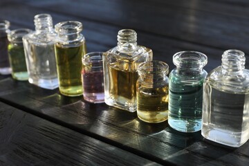 Perfume bottles with aromatic oils on black wooden background, closeup