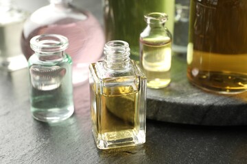 Open perfume bottles with aromatic essential oils on dark textured table, closeup