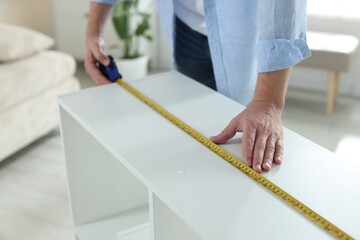 Man measuring white shelving unit with tape indoors, closeup