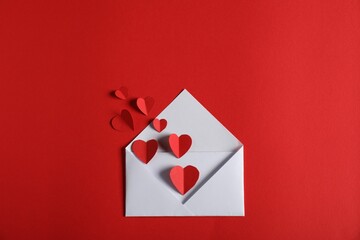 Paper hearts flying out of envelope on red background, flat lay