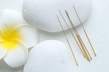 Acupuncture needles, spa stones and flower on white background, flat lay