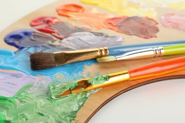 Wooden palette with paints and brushes on white background, closeup