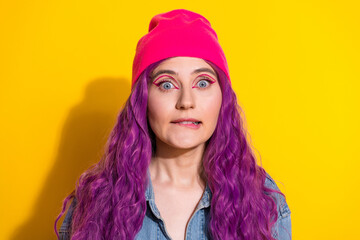 Portrait of a stylish young woman with purple dyed hair and a pink beanie posing against a bright yellow background