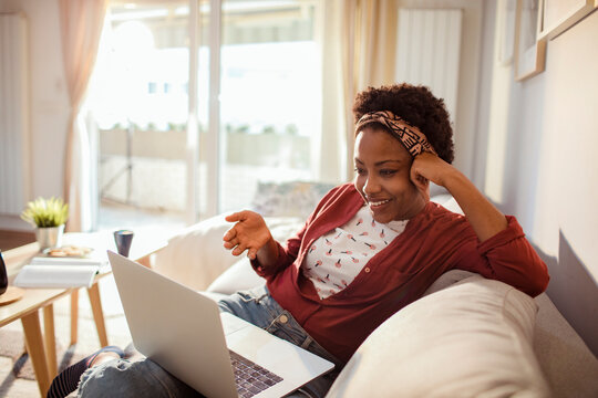 Young woman smiling while video chatting on laptop from cozy living room couch