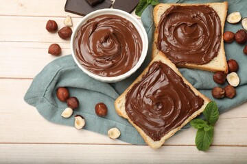 Toasts with chocolate hazelnut spread, nuts and mint on wooden table, flat lay