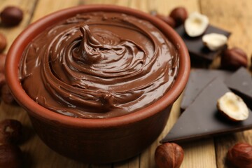 Tasty hazelnut spread, chocolate pieces and nuts on wooden table, closeup