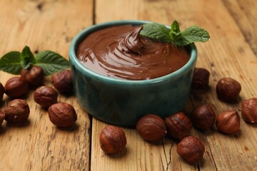 Tasty chocolate hazelnut spread with mint and nuts on wooden table, closeup