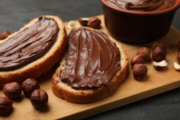 Toasts with tasty chocolate hazelnut spread and nuts on black table, closeup