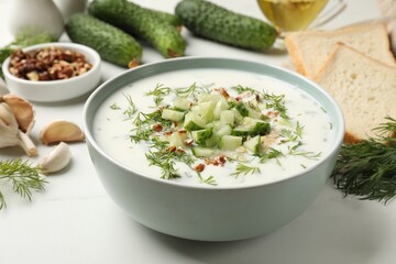 Tasty cucumber soup with dill and nuts in bowl on white table, closeup