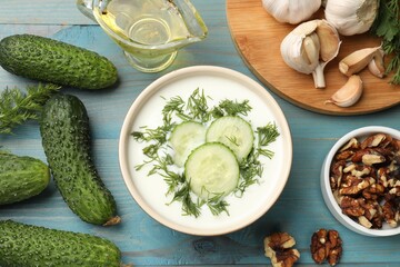 Tasty cucumber soup with dill among products on light blue wooden table, flat lay