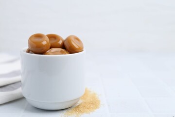 Tasty sweet caramel candies on white tiled table, closeup. Space for text