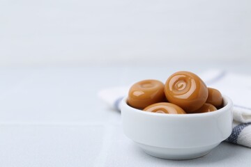Tasty sweet caramel candies on white tiled table, closeup. Space for text