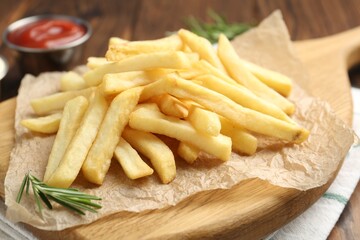 Tasty french fries served with ketchup and rosemary on wooden table, closeup