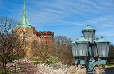 A church in the University Circle district of Cleveland Ohio stands above flowering cherry trees and an ornamental lamp post on a bright spring morning.
