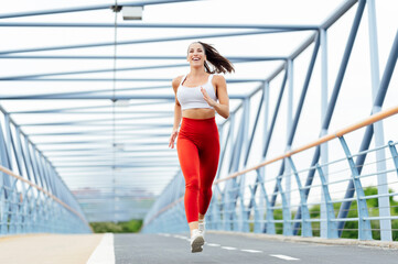 Fit woman jogging on a modern bridge during a sunny day