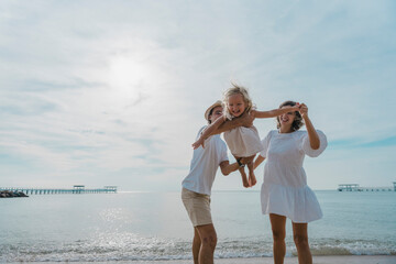 Happy parents with young children playing airplane running and flying on the beach joyfully, adventurous family on vacation