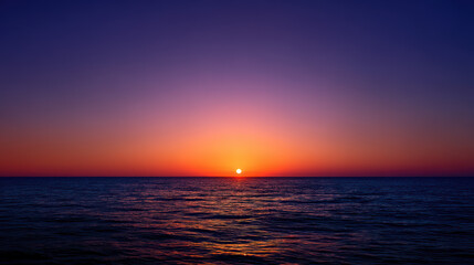 Fototapeta premium A stunning sunset paints the ocean with vibrant orange and purple hues, creating a peaceful and mesmerizing scene as the sun dips below the horizon line.