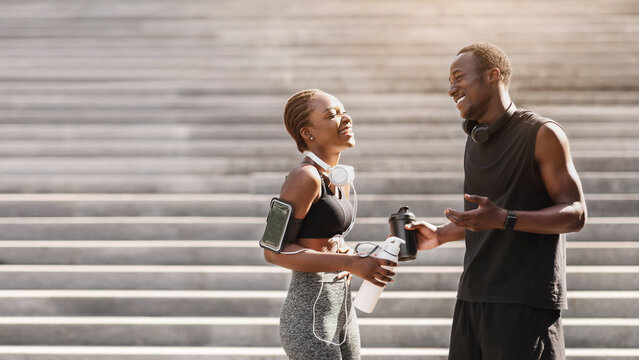 Joyful Black Runner Couple In Sportswear Resting After Training Outdoors, Chatting And Laughing Together, Free Space