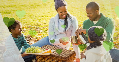 Image of green hearts over picnic basket and african american family in park