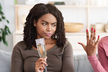 Happy black woman showing her upset and jealous girlfriend engagement ring. Annoyed african...