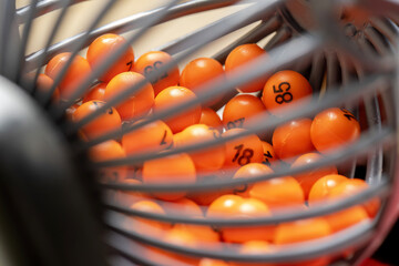 Extreme closeup of orange numbered lottery balls inside a spinning cage, concept of random chance, bingo game, gambling, drawing system or raffle mechanism, colorful abstract background, no people