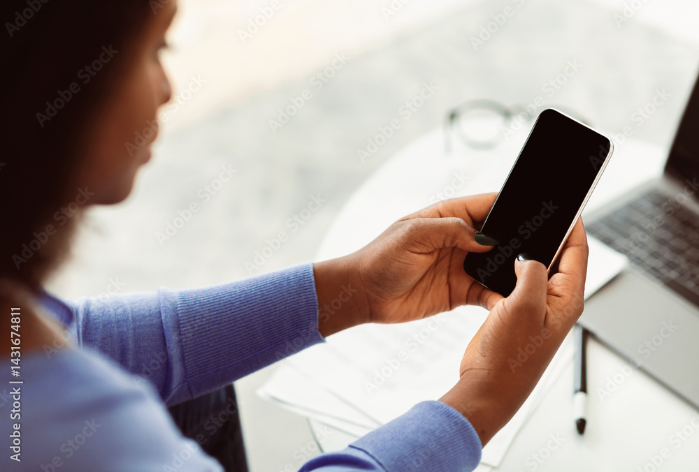 Poster unrecognizable black woman using cell phone with empty screen sitting at workplace. selective focus,