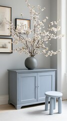 Minimalist living room features a light blue stool, gray cabinet, and white vases with flowers, creating a cozy and serene atmosphere