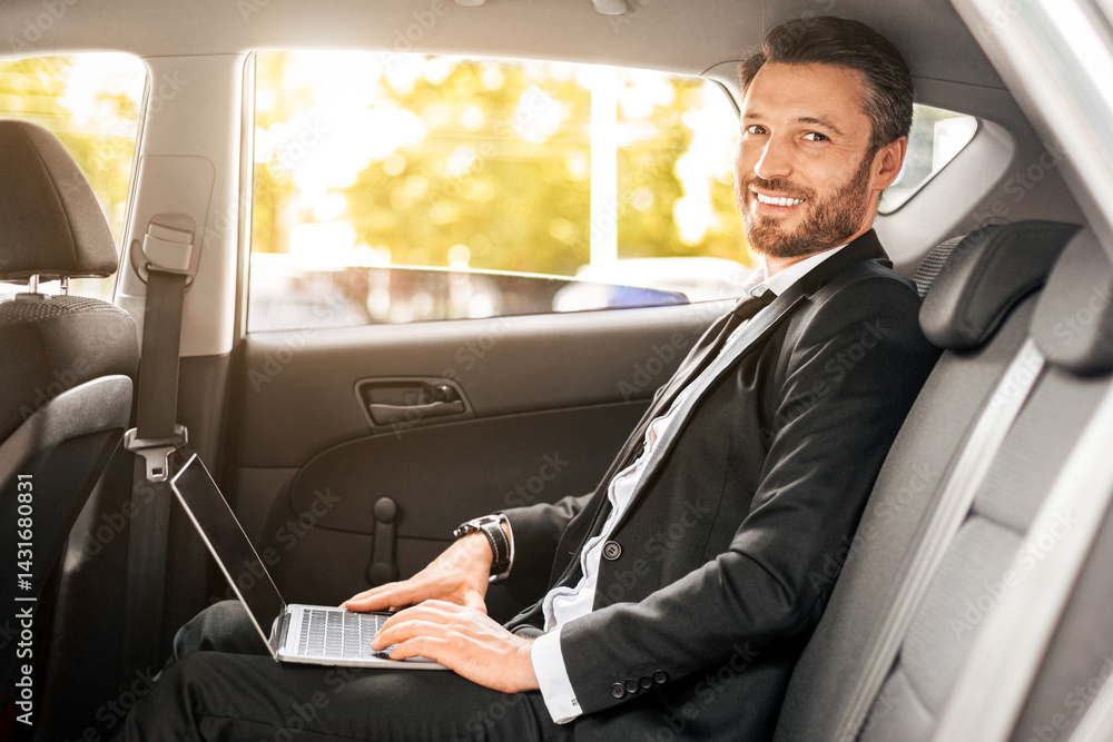 Poster cheerful businessman sitting in car, using laptop, working online. handsome man in suit working on n