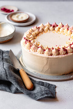 A beautifully decorated cake with cream frosting and colorful sprinkles on a light background, accompanied by a knife and a gray linen cloth.