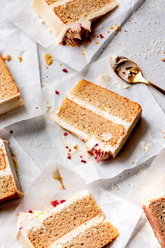 Slices of layered cake with frosting on parchment paper, accompanied by a gold spoon.