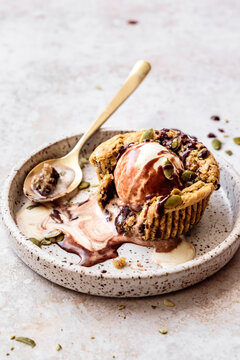 A dessert featuring ice cream served in a cookie cup with chocolate sauce and pumpkin seeds on a speckled plate.