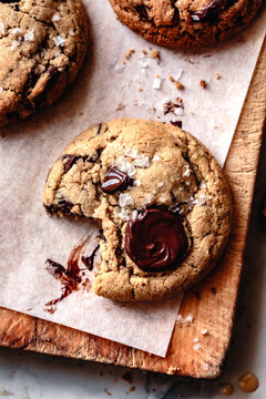 An assortment of freshly baked cookies with chocolate chunks and sea salt, displayed on a wooden board.