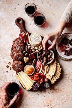 An inviting charcuterie board featuring a variety of cheeses, cookies, fruits, nuts, and chocolates, accompanied by glasses of red wine.