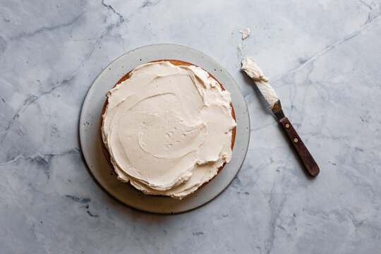 A cake with creamy frosting on a marble surface, accompanied by a butter knife.