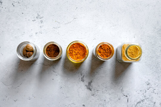 Five jars containing different spices are arranged in a line on a textured surface.