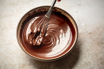 A bowl of chocolate batter being whisked on a light countertop.