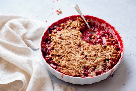 A freshly baked berry crumble pie with a portion missing, served in a white dish with a spoon and a linen cloth nearby.