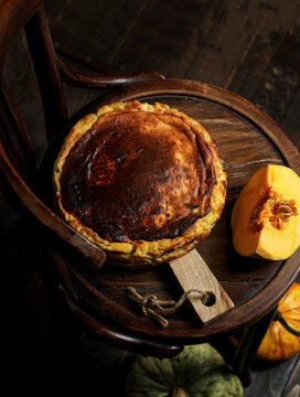 Basque pumpkin cheesecake on a dark vintage chair, rustic and moody autumn aesthetic