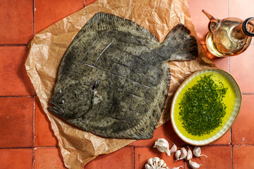 turbot flounder on a rustic wooden cutting board with olive oil, garlic, and green sauce on a tile background