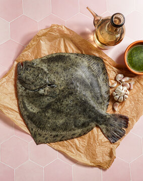 turbot flounder on a rustic wooden cutting board with olive oil, garlic, and green sauce on a tile background