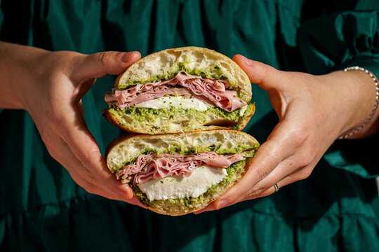 delicious  Italian Mortadella Sandwich with Pesto and Mozzarella basil pesto, crusty ciabatta bread, in the hands, against a deep green fabric background