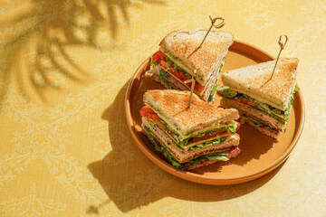 club sandwich served on a wooden cutting board. The sandwich is layered with crispy toasted bread, fresh lettuce, ripe tomatoes, slices of ham, and cheese