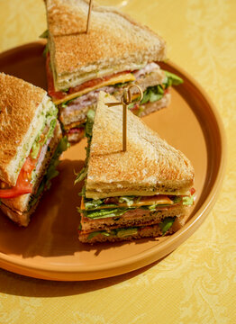 club sandwich served on a wooden cutting board. The sandwich is layered with crispy toasted bread, fresh lettuce, ripe tomatoes, slices of ham, and cheese
