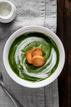 Bowl of spinach cream placed on a wooden table. On the surface of the cream, golden croutons are carefully arranged, creating a captivating contrast of both color and texture.