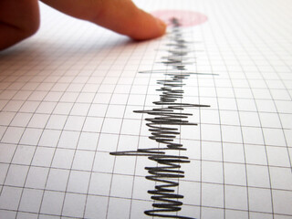    Seismograph and earthquake. A hand pointing at a seismograph recording the seismic activity of an earthquake                           