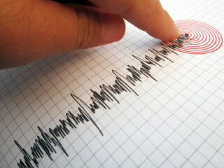 Seismograph and earthquake. A hand pointing at a seismograph recording the seismic activity of an earthquake	