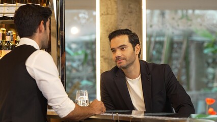 Smiling smart VIP customer sitting at counter bar talking with bartender back side making great first impression neat professional barman costume recommending drink list at nightclub luxury. Vinosity.