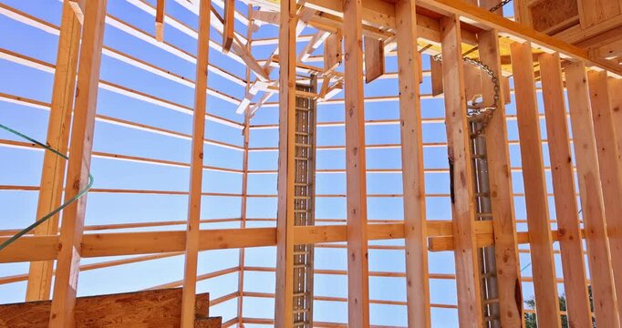 Detailed wooden roof framing with exposed beams, ladder, blue sky background. Construction site with structural framework in progress.