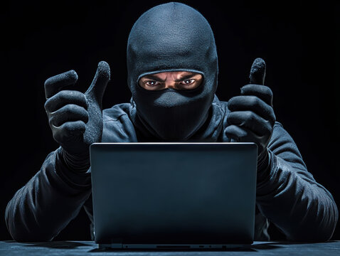 Masked hacker celebrating success at laptop in dark environment