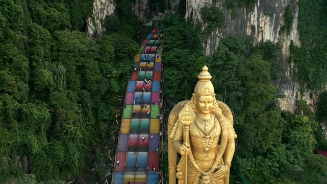 Aerial view of Batu Caves and golden Lord Murugan statue in Kuala Lumpur, Malaysia. Famous religious landmark with colorful stairs, limestone cliffs, and lush greenery.